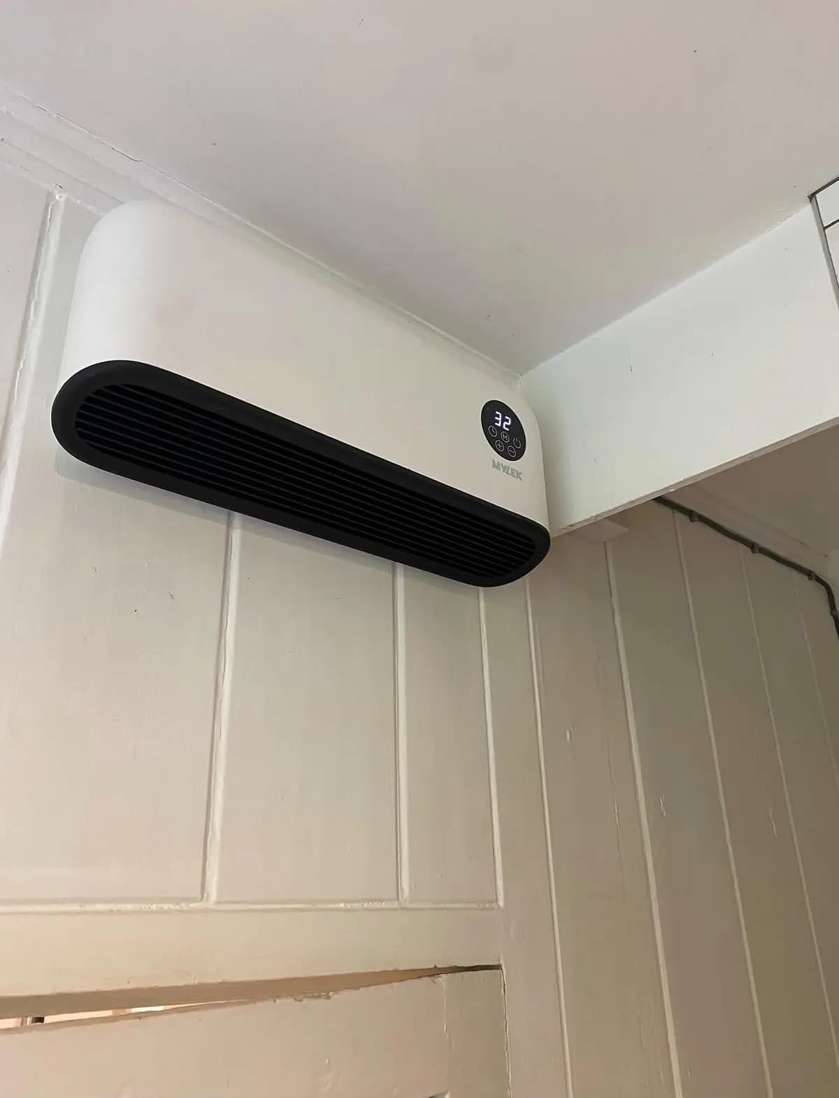 Wall-mounted bathroom fan heater installed high on a panelled wall in Redhill